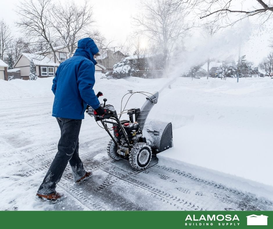 Man wearing winter gear using snowblower to clear driveway
