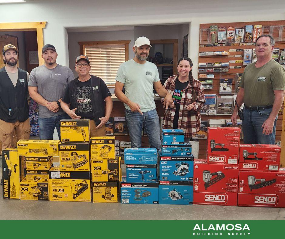 Group of Alamosa Building Supply staff standing behind a display of DeWalt, Makita, and Senco tool boxes inside the store.